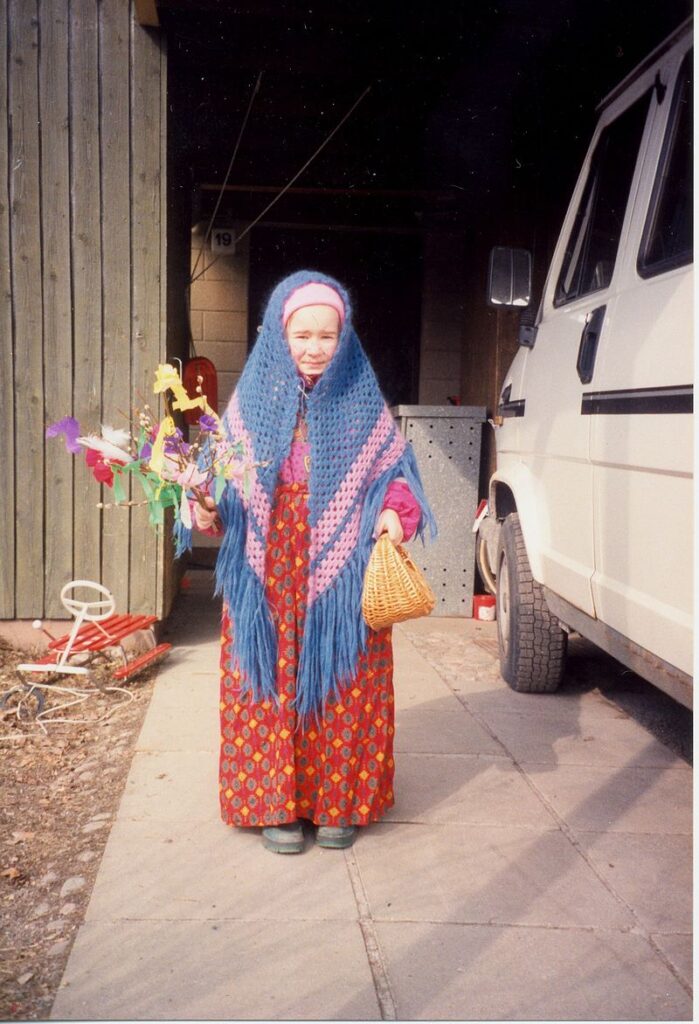 A child dressed up as a witch, holding decorated pussy willow branches and a wicker basket.